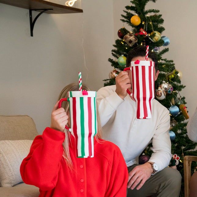 Five people in a living room with Christmas decorations, holding colorful mugs and socks.