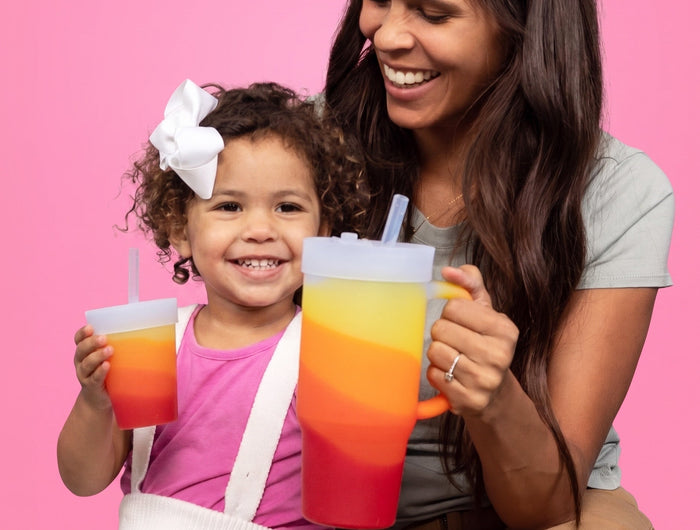 Woman and child holding colorful drinks against a pink background