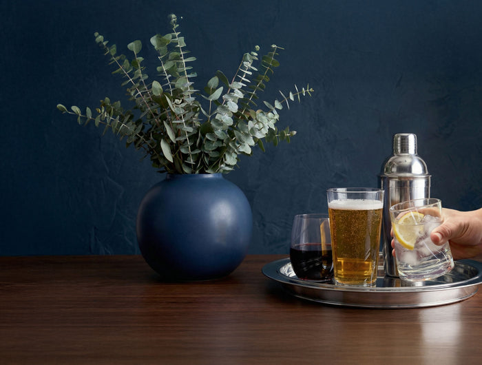 Tray with drinks and a cocktail shaker on a wooden table against a dark blue wall.