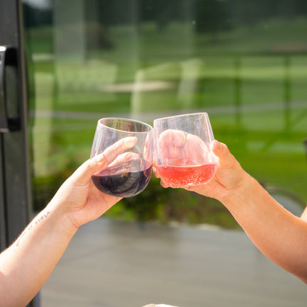 Two women toasting with glasses of red and pink drinks outdoors.