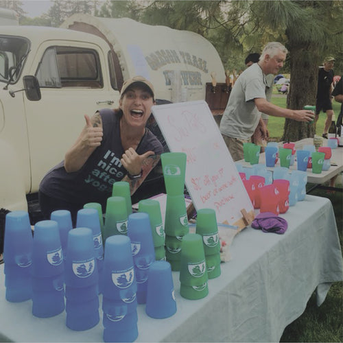 Woman with a table full of Silipints with logos. Being used as giveaways at an event.